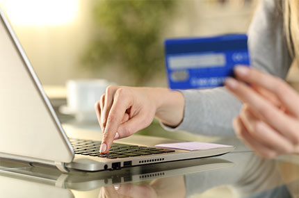 Close up of woman typing on laptop while holding a credit card