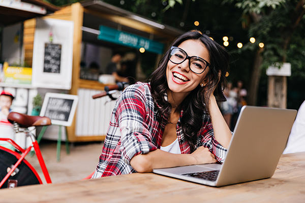 Woman using laptop at cafe while smiling and looking into the camera