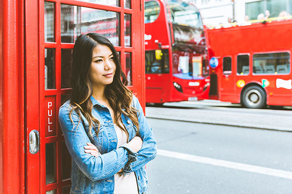 Woman standing next to red telephone booth with buses in the background in the UK